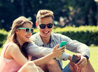 Image showing smiling friends with smartphones sitting in park