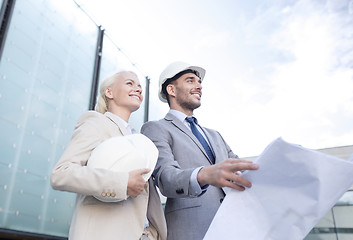 Image showing smiling businessmen with blueprint and helmets