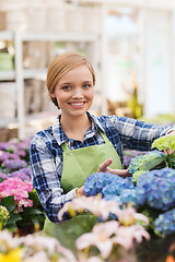 Image showing happy woman taking care of flowers in greenhouse