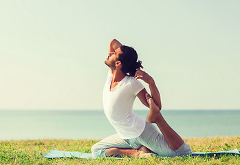 Image showing smiling man making yoga exercises outdoors