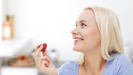 Image showing happy woman eating strawberry on kitchen