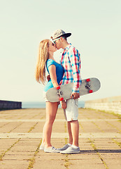 Image showing smiling couple with skateboard kissing outdoors