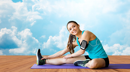 Image showing smiling woman stretching leg on mat over clouds