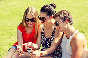 Image showing smiling friends with smartphones sitting in park