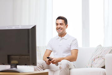 Image showing smiling man with remote control watching tv