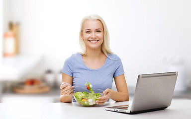 Image showing smiling woman eating salad with laptop on kitchen