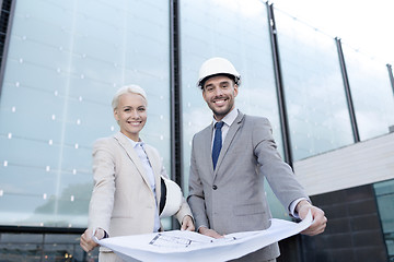 Image showing smiling businessmen with blueprint and helmets