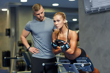 Image showing woman with personal trainer flexing muscles in gym