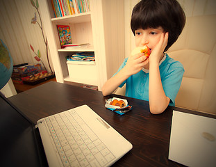 Image showing pensive boy sitting with a laptop and eating apple