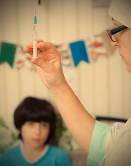 Image showing Doctor pediatrician with a syringe and a child in the background