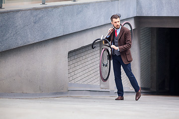 Image showing Handsome businessman carrying his bicycle