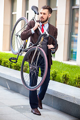 Image showing Handsome businessman carrying his bicycle