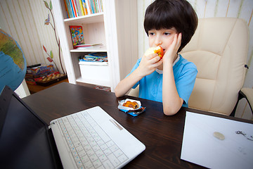 Image showing pensive boy sitting with a laptop and eating apple