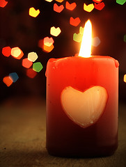 Image showing Red candle on the table and shiny hearts in background.