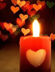 Image showing Red candle on the table and shiny hearts in background.