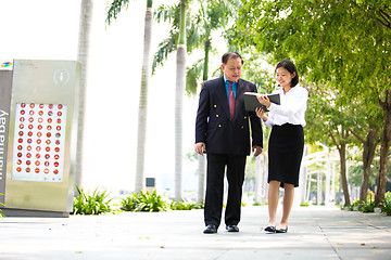 Image showing Young Asian female executive and senior businessman walking together