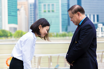 Image showing Young Asian female executive and senior businessman in suit bowing to each other
