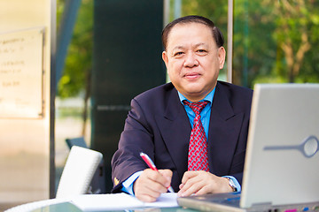 Image showing Senior Asian businessman in suit writing proposal