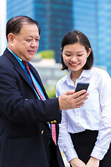 Image showing Young Asian female executive and senior businessman using smart phone