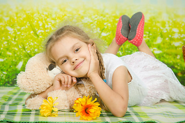 Image showing Five-year girl hugging a teddy bear lying on picnic rug