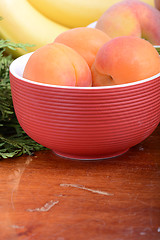 Image showing bananas and apricots on red plate, close up