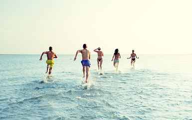 Image showing smiling friends running on beach from back