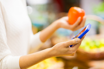 Image showing woman with smartphone and persimmon in market