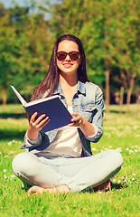 Image showing smiling young girl with book sitting in park