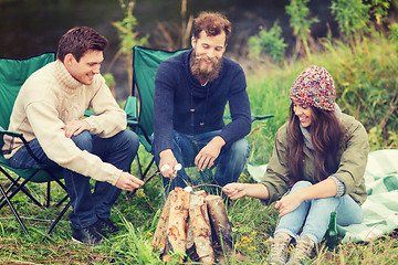 Image showing smiling tourists cooking marshmallow in camping