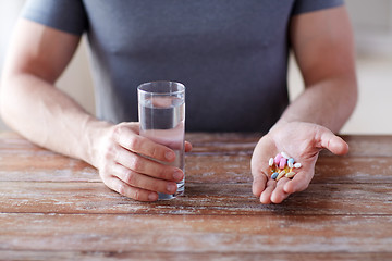 Image showing close up of male hands holding pills and water