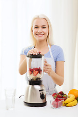 Image showing smiling woman with blender preparing shake at home