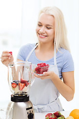 Image showing smiling woman with blender preparing shake at home