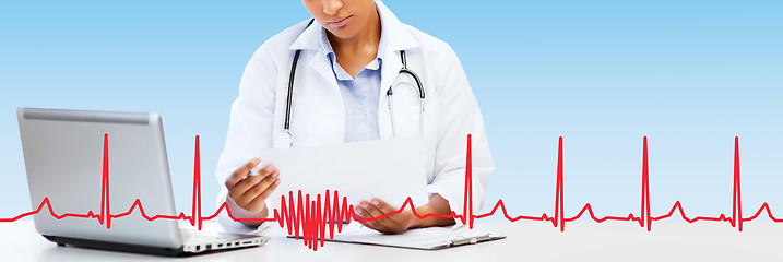 Image showing female doctor with laptop pc looking at paper