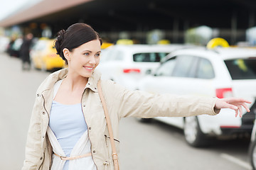 Image showing smiling young woman waving hand and catching taxi