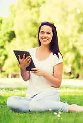 Image showing smiling young girl with tablet pc sitting on grass