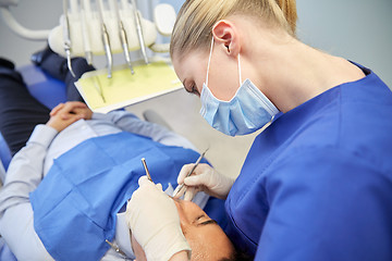 Image showing female dentist in mask checking male patient teeth