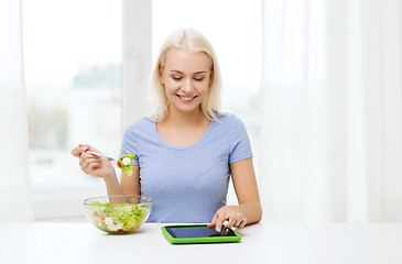 Image showing smiling woman eating salad with tablet pc at home