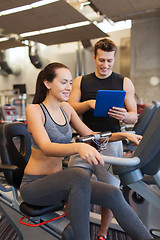 Image showing happy woman with trainer on exercise bike in gym