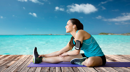 Image showing smiling woman stretching leg on mat over sea