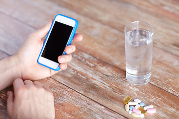 Image showing close up of hands with smartphone, pills and water