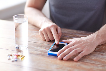 Image showing close up of hands with smartphone, pills and water