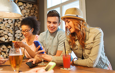 Image showing happy friends with smartphones and drinks at bar