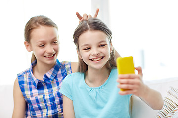 Image showing happy girls with smartphone taking selfie at home