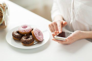 Image showing close up of hands with smart phone and donuts