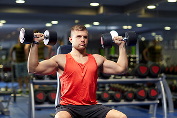 Image showing young man with dumbbells flexing muscles in gym