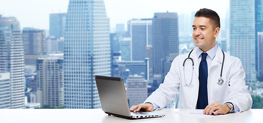 Image showing smiling male doctor with laptop sitting at table