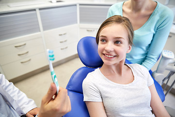 Image showing happy dentist showing toothbrush to patient girl