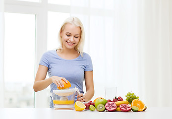 Image showing smiling woman squeezing fruit juice at home