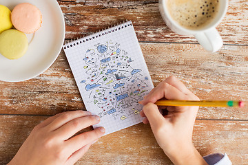 Image showing close up of hands drawing scheme to notebook