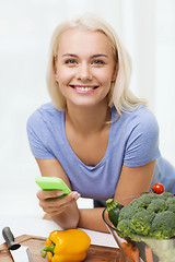 Image showing smiling woman with smartphone cooking vegetables